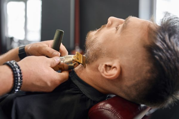 Brunette male on procedure of cutting beard in barbershop.